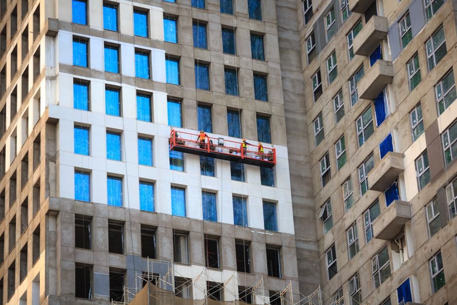 Construction workers installing modern glass facade on a vertical housing project