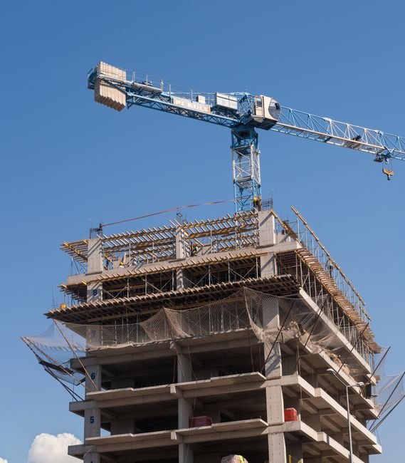 heavy crane lifting large precast concrete panel on building construction site