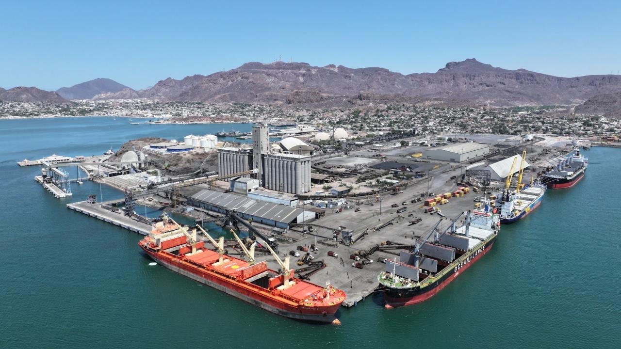 Vista aérea del puerto de Guaymas con buques de carga atracados, silos y la sierra al fondo