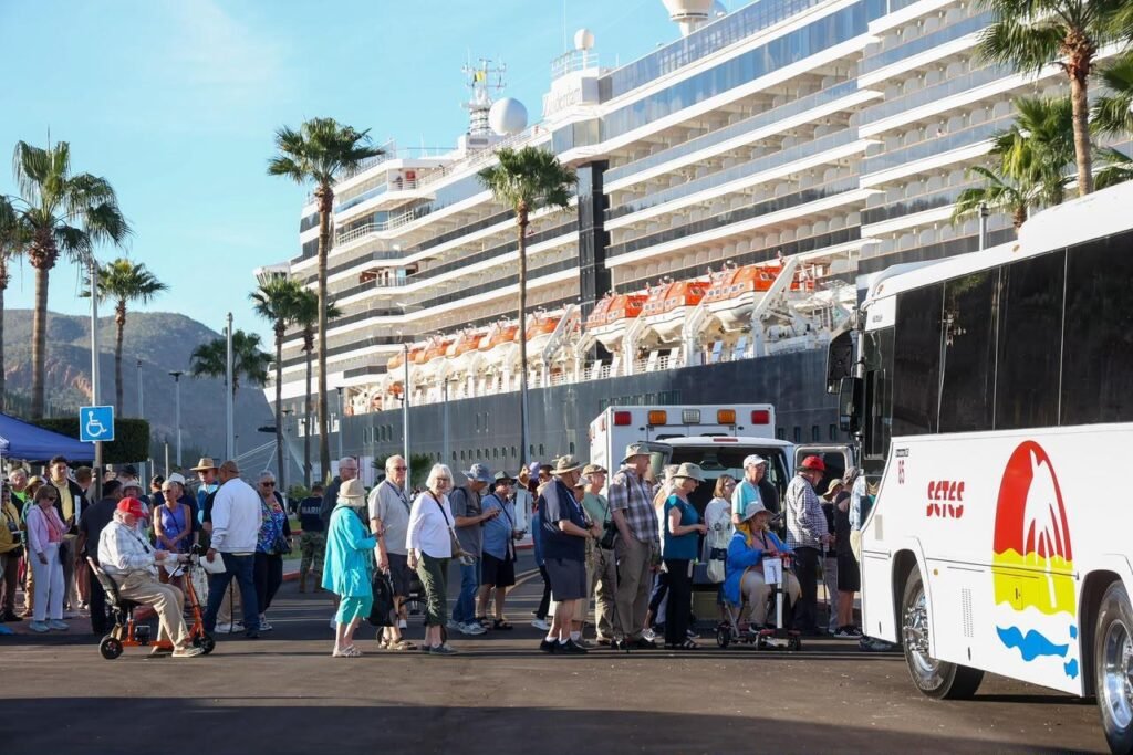 Pasajeros de un crucero atracado en Guaymas caminan hacia autobuses turísticos entre palmeras