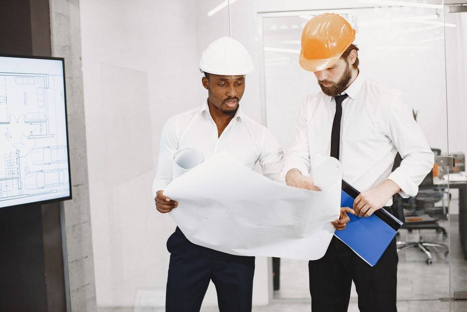 Engineers reviewing modern industrial building blueprints with hardhats on site