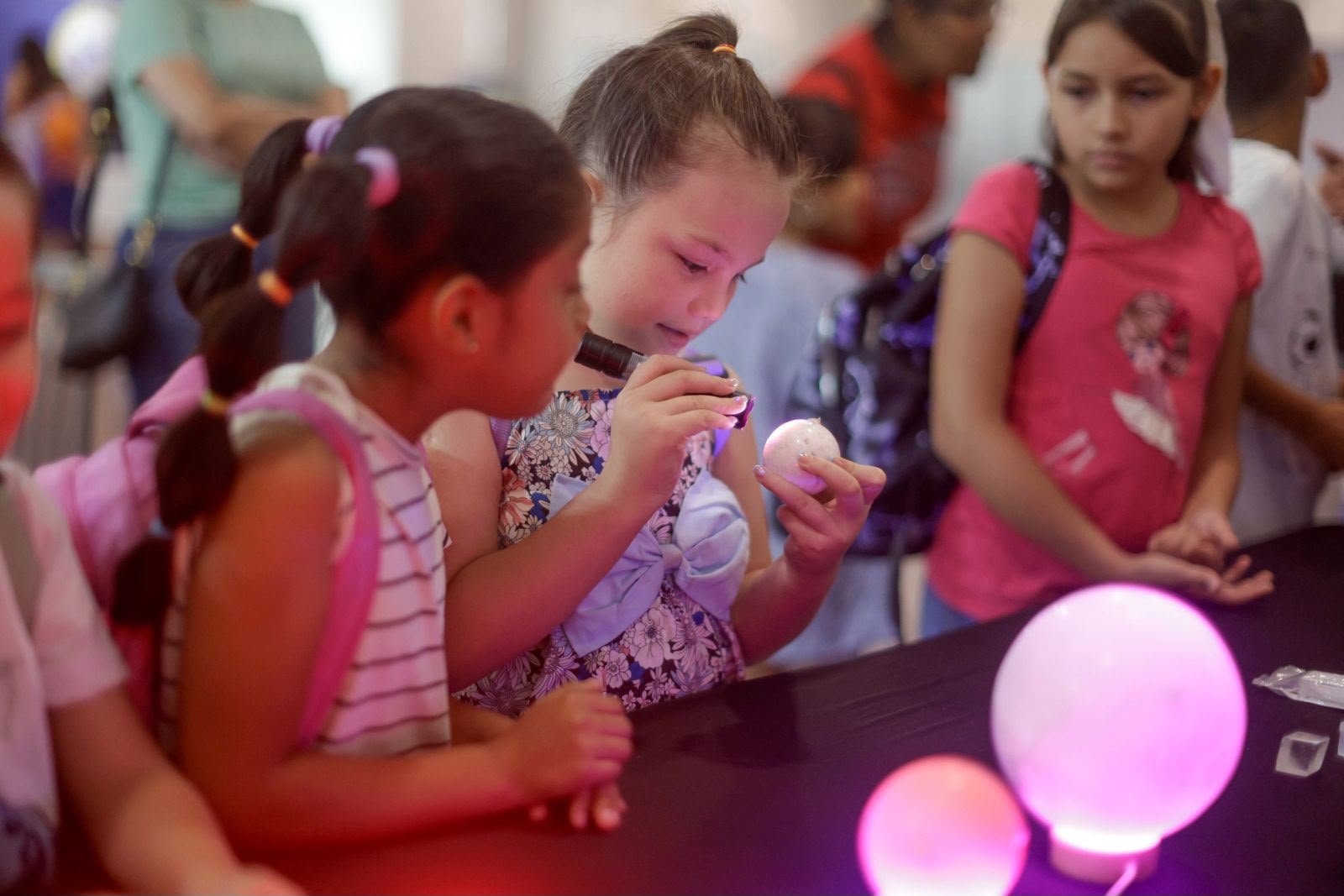 Dos niñas observan con lupa una muestra de mineral iluminada durante el recorrido