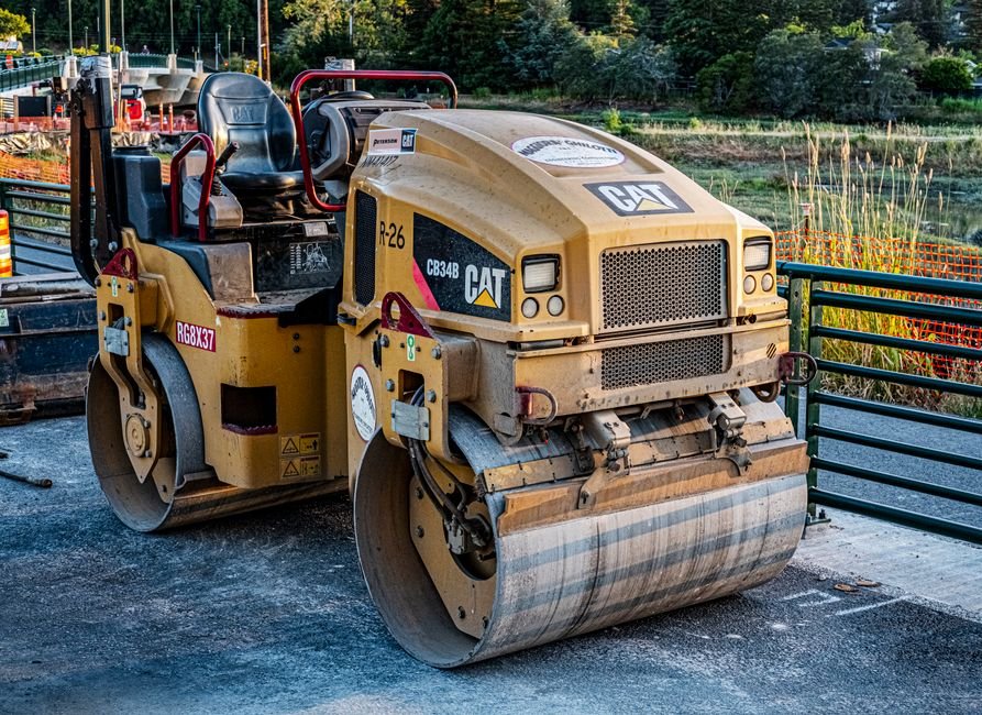 Heavy machinery compacting fresh asphalt on a sunny road construction site