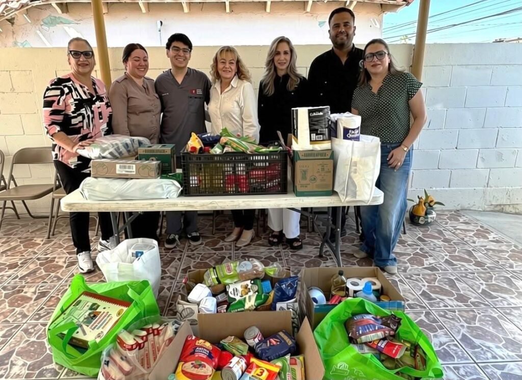Grupo de personas detrás de una mesa con víveres, artículos de limpieza y bolsas con despensa.