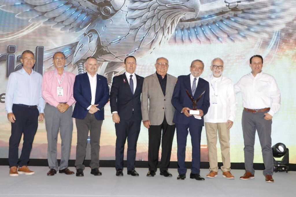 Ocho hombres posan sobre el escenario; uno de ellos sostiene el trofeo con forma de águila.