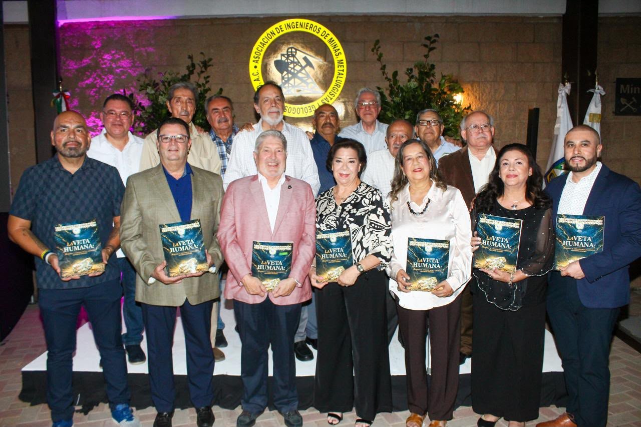 Grupo de personas de pie sostiene ejemplares del libro “La Veta Humana” frente al escudo de la AIMMGM Distrito Sonora.