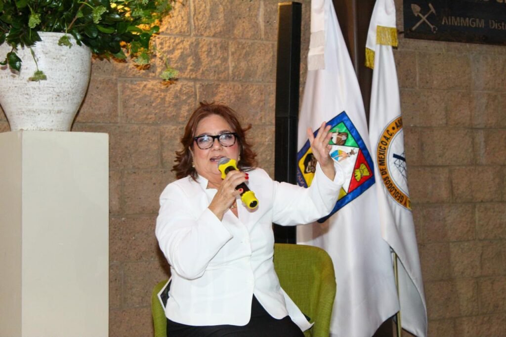 Mujer con blusa blanca habla al micrófono sentada en el escenario.