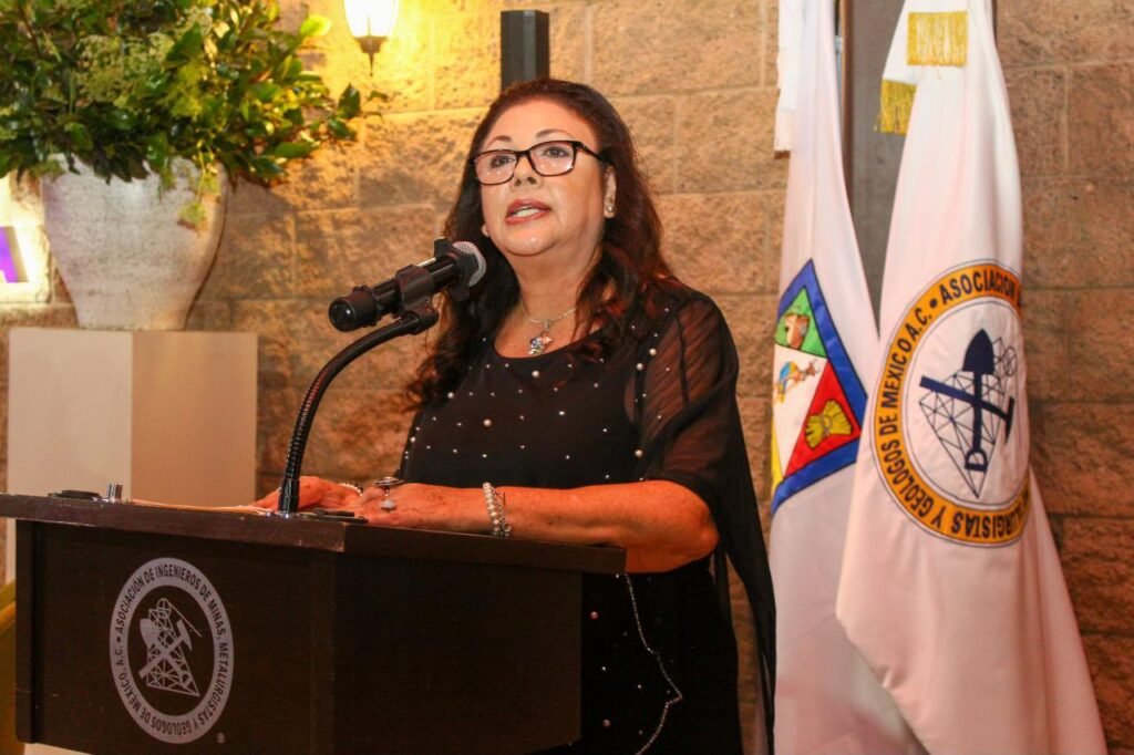 Mujer vestida de negro habla desde el atril junto a banderas de la asociación.