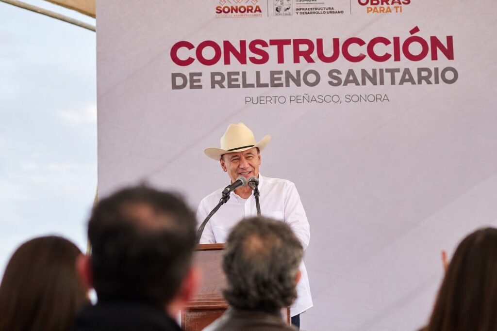 Hombre con sombrero y camisa blanca habla en un atril frente a una lona con la leyenda «Construcción de relleno sanitario, Puerto Peñasco, Sonora».